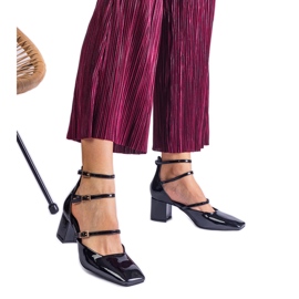 Schwarze Pumpen, die auf einem Pfosten mit Schnallen lackiert sind