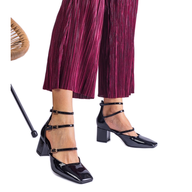 Schwarze Pumpen, die auf einem Pfosten mit Schnallen lackiert sind