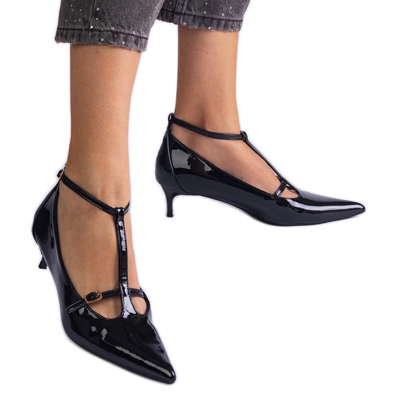 Schwarze Pumpen, die auf einem niedrigen Stapel mit Schnallen lackiert sind