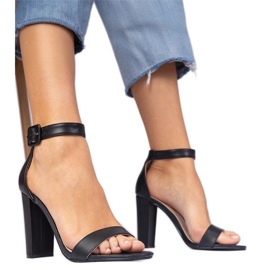 Schwarze Sandalen auf dem Pfosten, der am Knöchel befestigt war