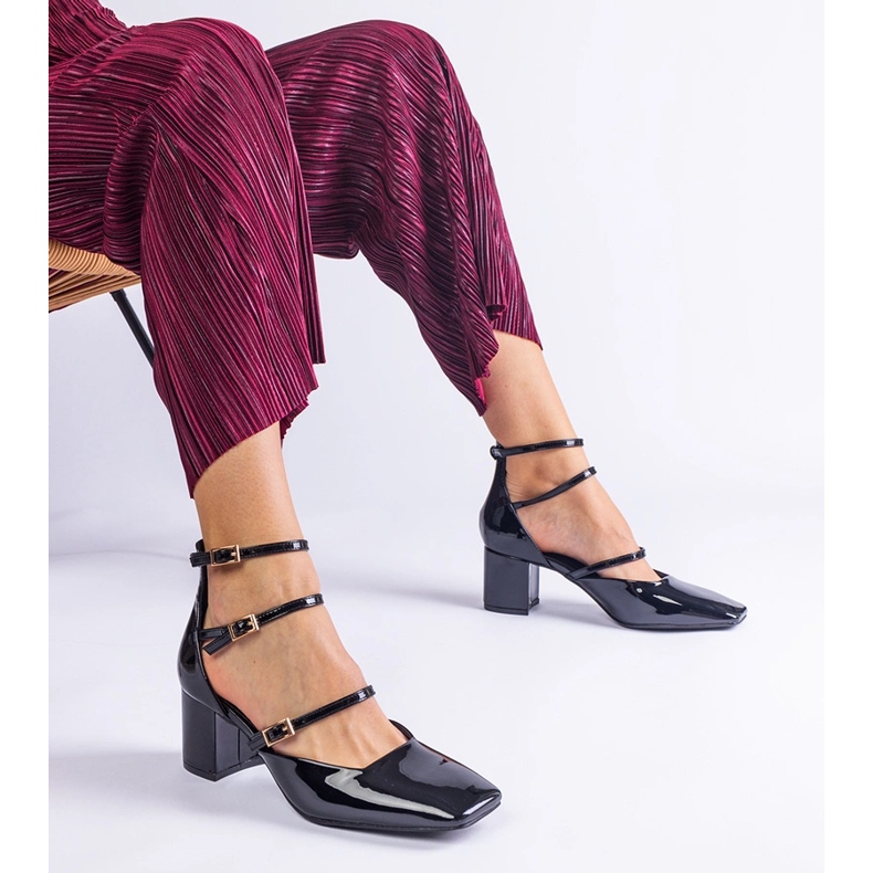 Schwarze Pumpen, die auf einem Pfosten mit Schnallen lackiert sind 1