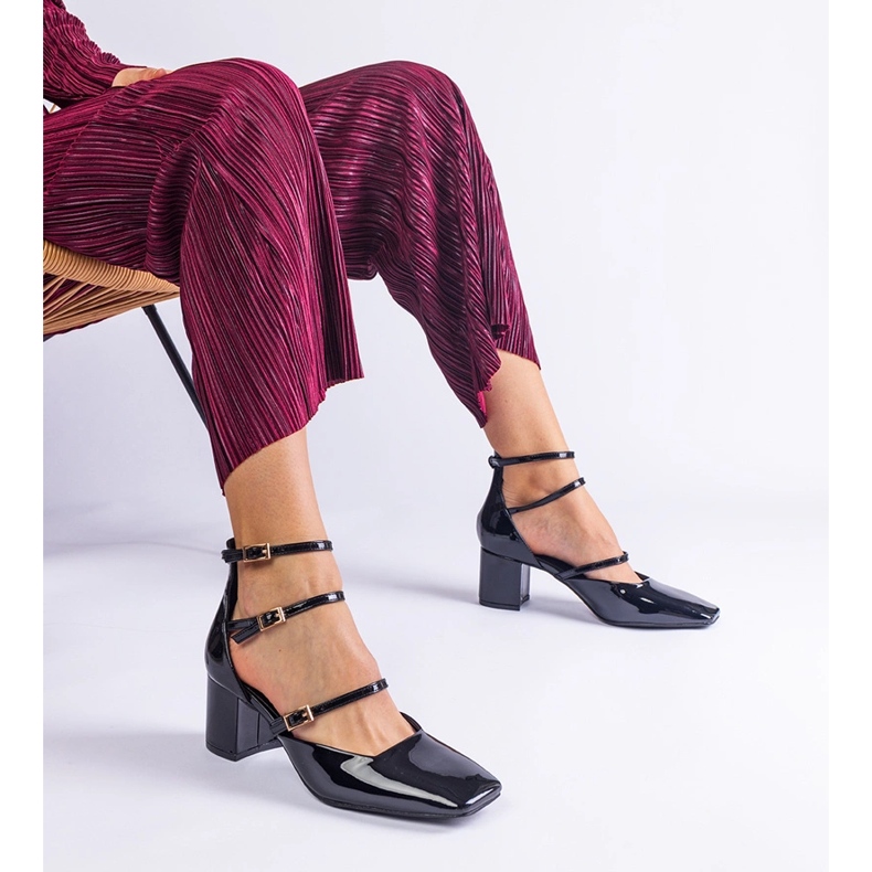 Schwarze Pumpen, die auf einem Pfosten mit Schnallen lackiert sind 2